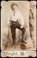 Albumen cabinet card portrait of a man with two six-guns, a rifle, and a ten-gallon hat