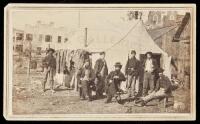 Carte-de-visite photograph of a soldier, 5 civilians (possibly Pinkerton Agents?), and an African American, standing or seated before a white camp tent