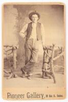 Cabinet card portrait of Californian in denim pants leaning against wood fence prop