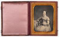 Daguerreotype portrait of seated woman wearing gloves and resting right arm on posing table