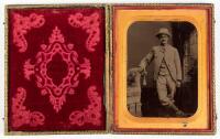 Tintype of standing gentleman wearing hat with right hand resting on arm of posing couch