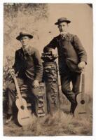 Tintype of two musicians, each with a harmonica and guitar in an elaborate posing set