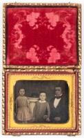 Daguerreotype portrait of seated gentleman with two children, hat on top of posing pedestal