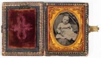 Ninth plate tintype of young baby posed in a dress and cradled in a blanket housed in a spray of flowers papier-mache case inlaid with mother-of-pearl.