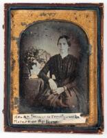 Daguerreotype portrait of woman seated with arm resting on posing table with flowers