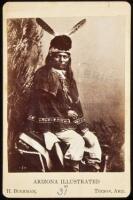 Photograph of Indian man seated in studio with two feathers in his hat