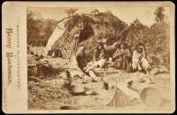 Photograph of a Pima Indian man, three women and a child seated in front of their thatched lodge