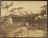 Albumen photograph of a young woman seated in a rock in a stream underneath a bridge