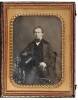 Daguerreotype of a man seated in studio, holding a large top hat and gloves