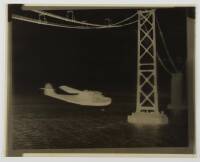 Photographic negative of a large flying boat under the San Francisco Bay Bridge during construction