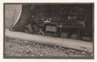 Vintage photograph of a Chinese man in a sidewalk fruit and herb stand smoking an opium pipe